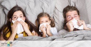 בני משפחה מצוננים במיטה, מקנחים את האף. חיסון נגד צינון ימנע מהם את זמן המשפחה הזה אבל יאפשר זמן כיפי יותר